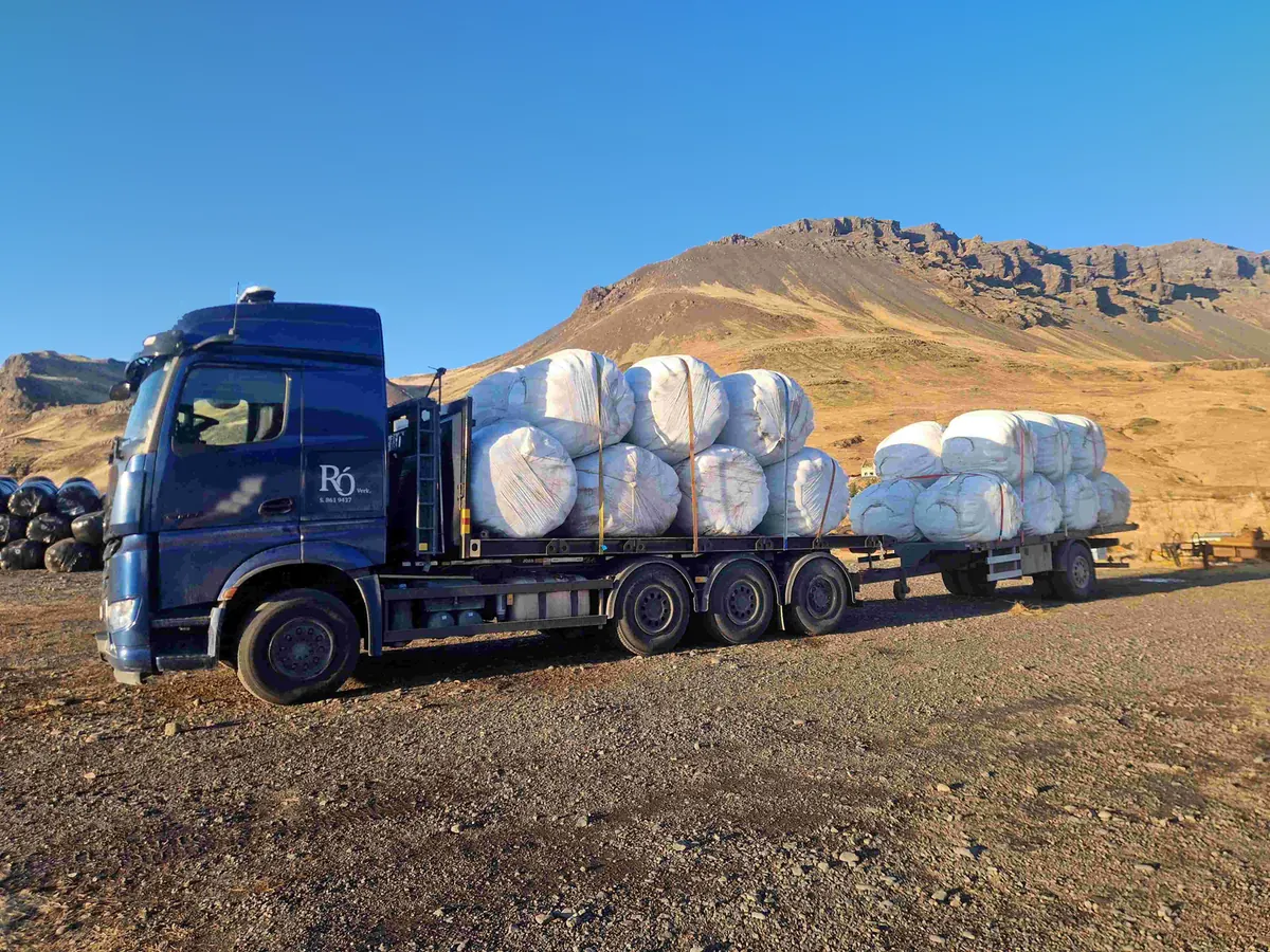 Blár vörubíll Þróttar með heyrúllur á palli og vagni