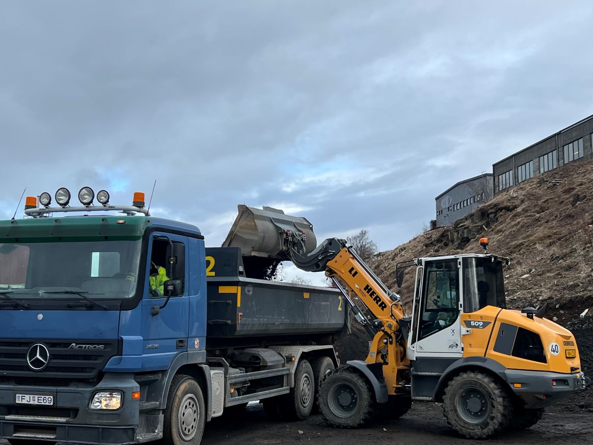 Blár vörubíll og gul Liebherr-hjólaskófla við jarðefnaafgreiðslu Þróttar