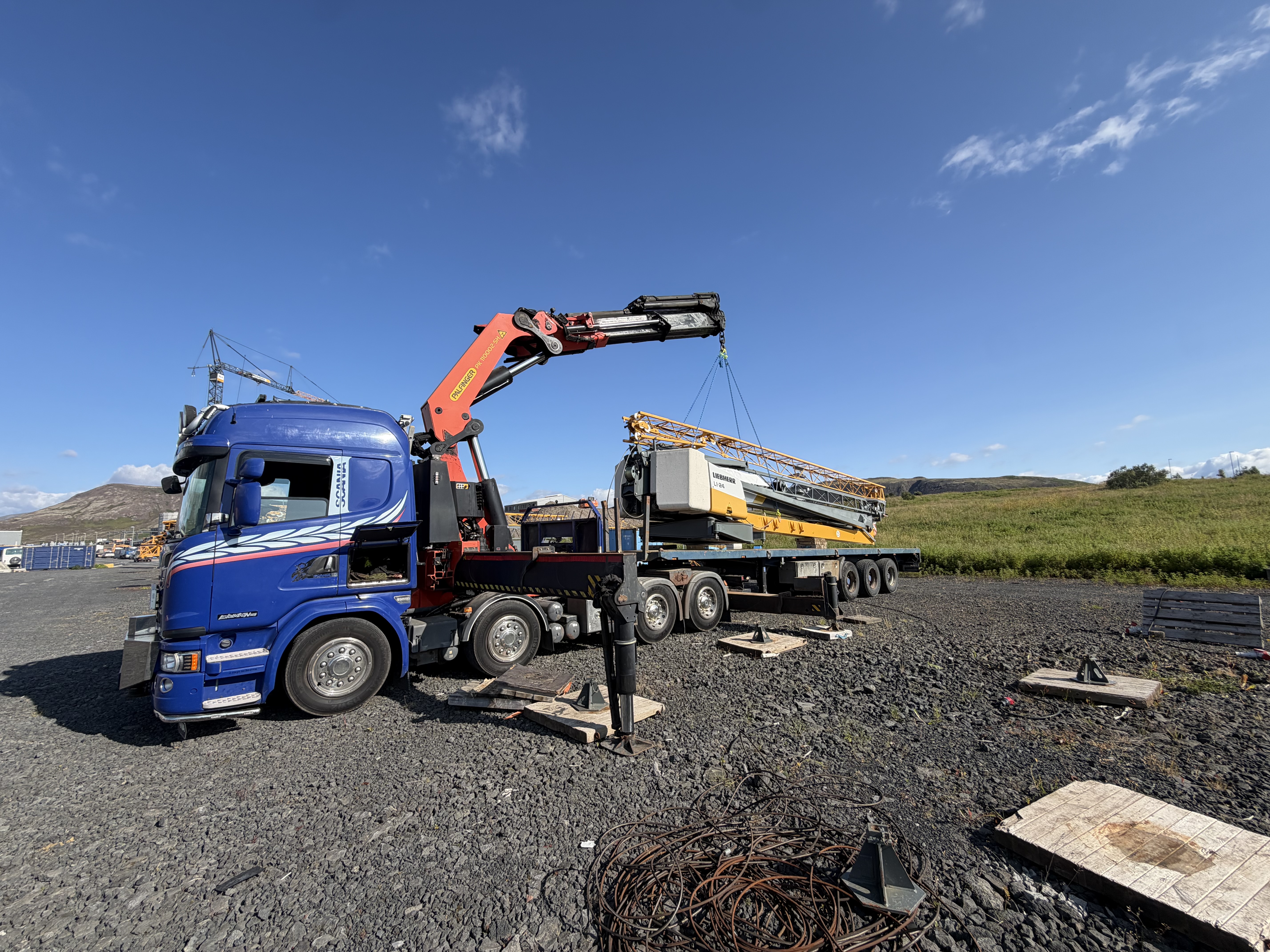 Blár kranabíll við byggingakrana á flutningavagni í björtu veðri.